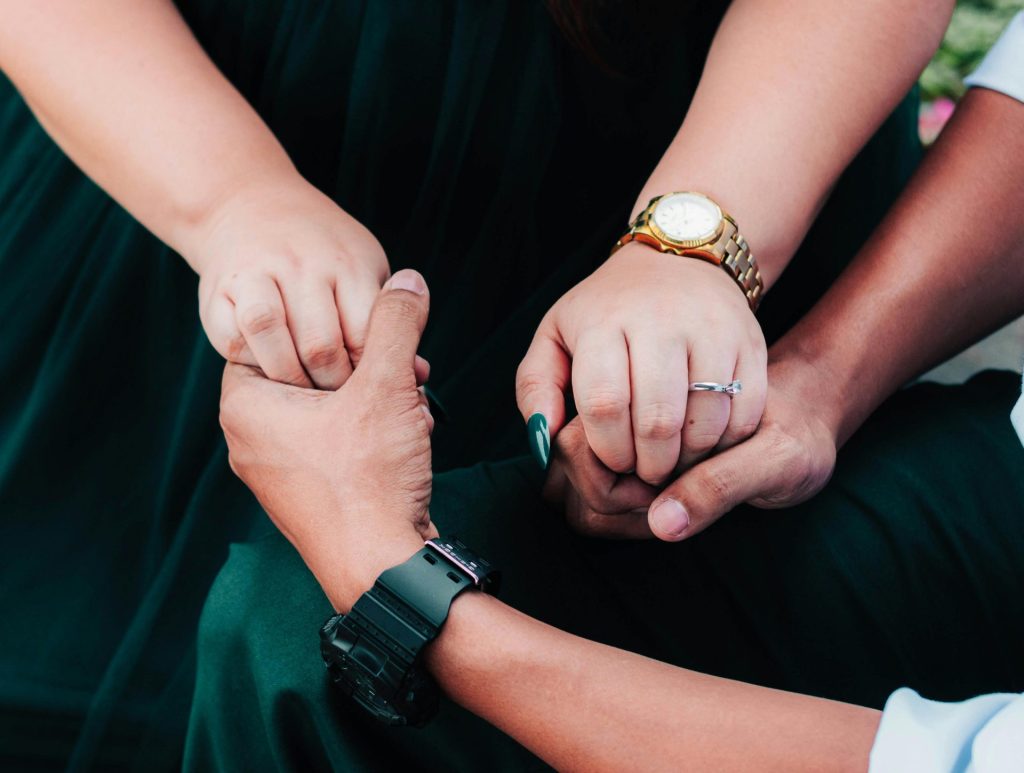 Close-up of intertwined hands symbolizing love and support with watches and rings visible.